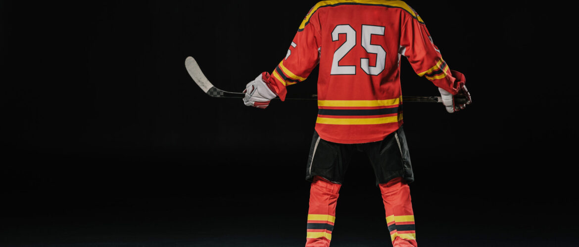 back view of professional ice hockey player holding hockey stick on black